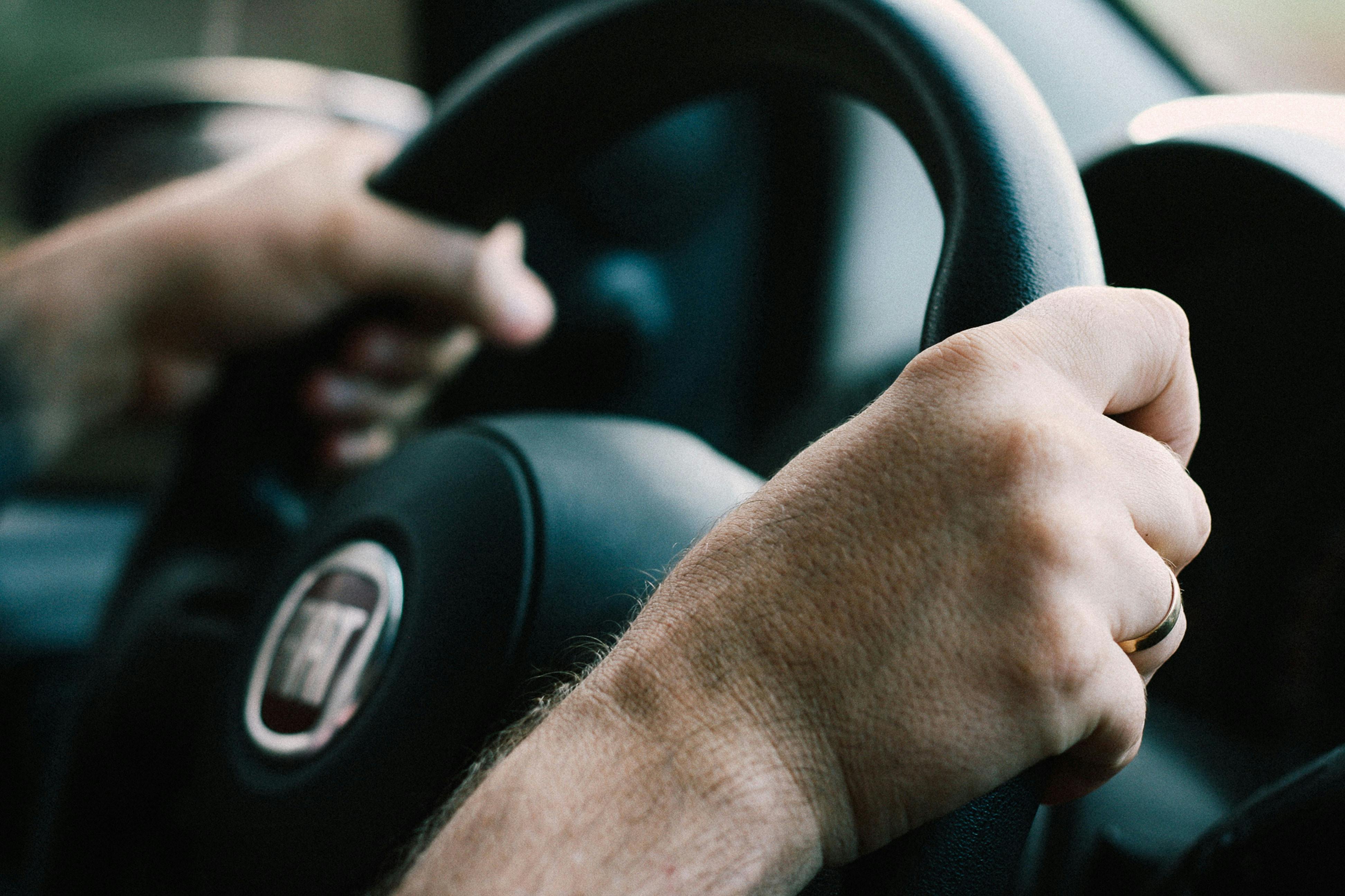 Hands resting on a car steering wheel while driving
