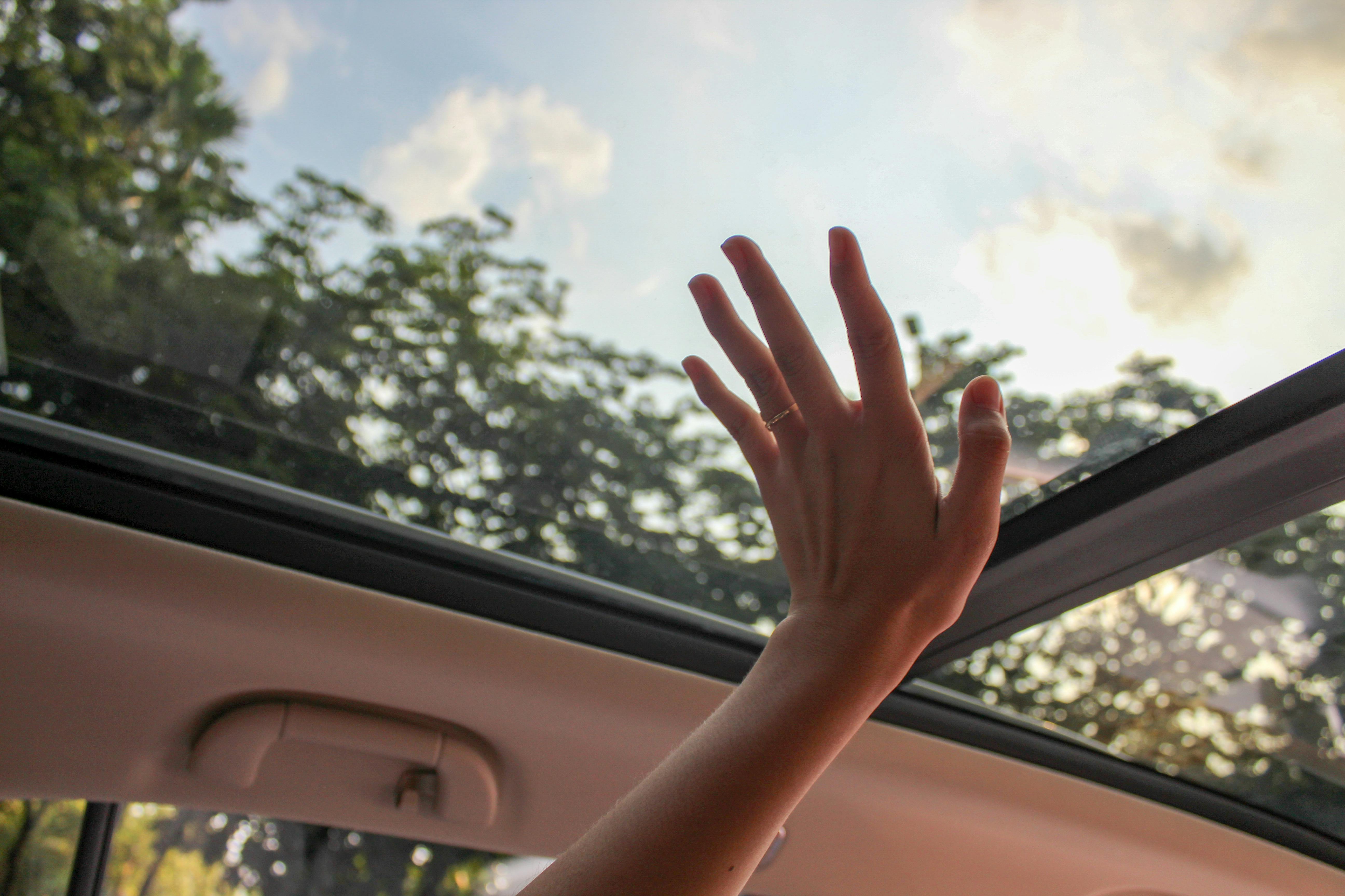 A hand reaching up through an open car sunroof towards the sky