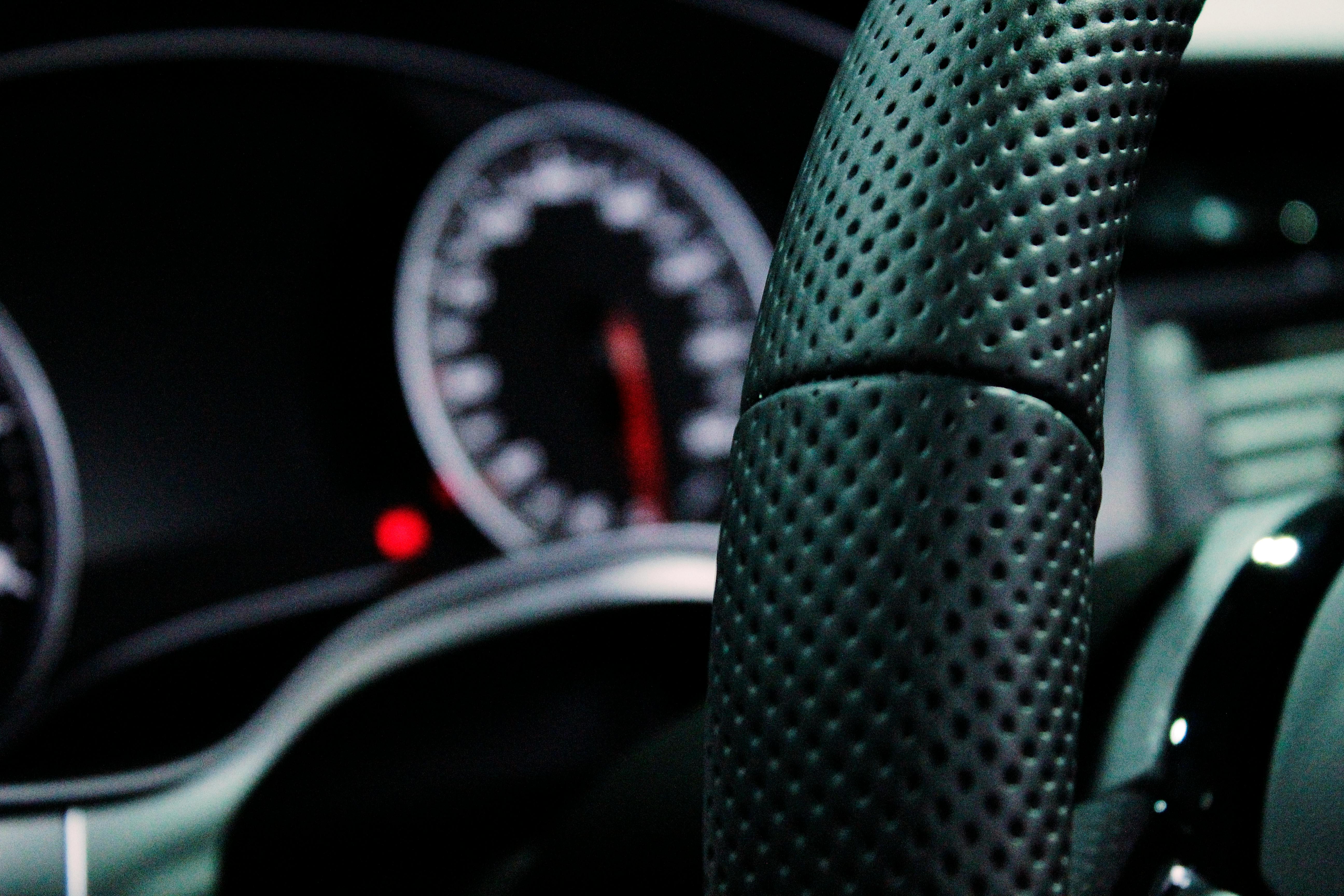 Close-up of a perforated leather steering wheel with the speedometer behind it