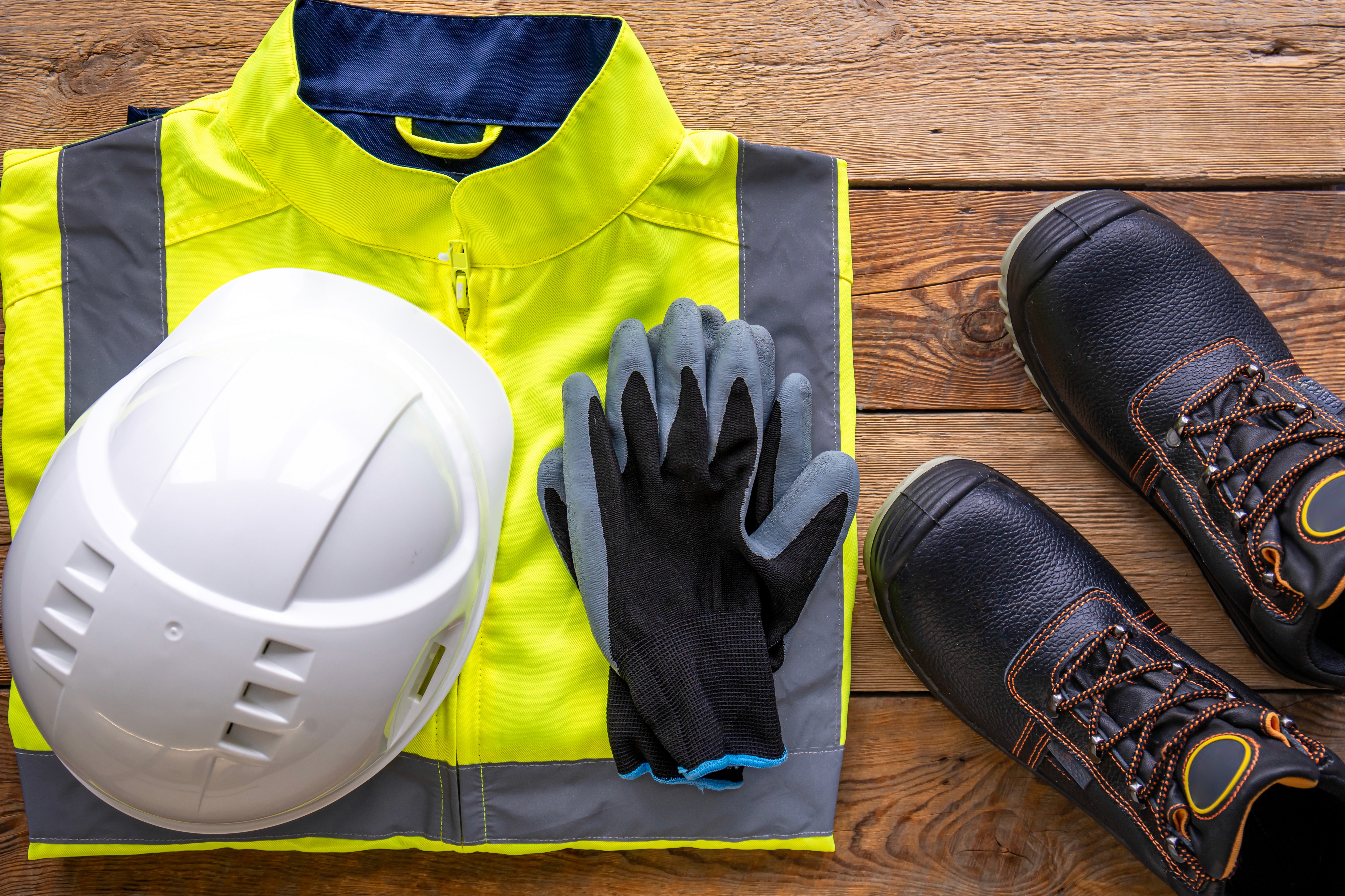 A hard hat, high-visibility jacket, gloves and work boots laid out