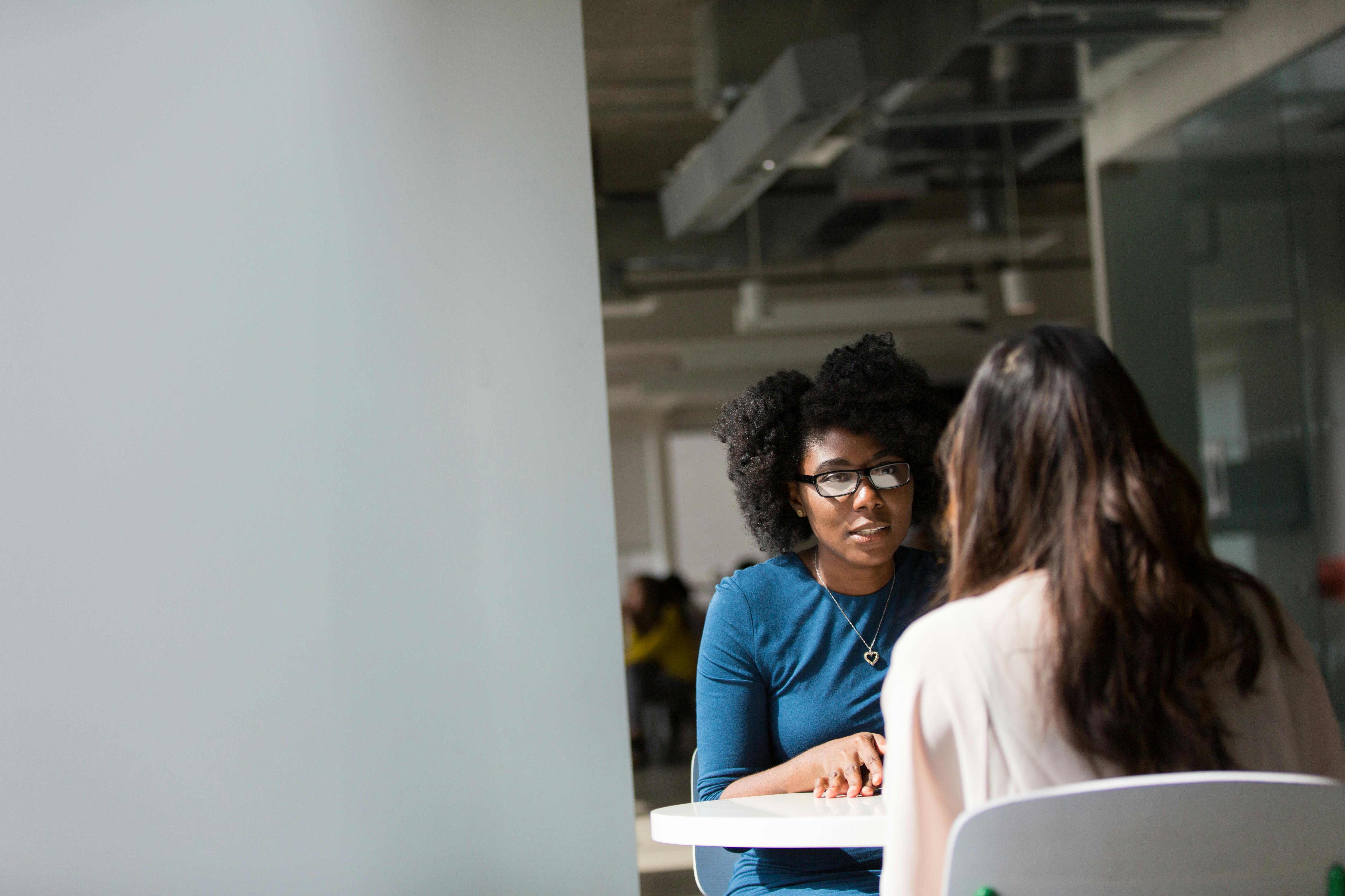 Two colleagues talking at a table in an open-plan office